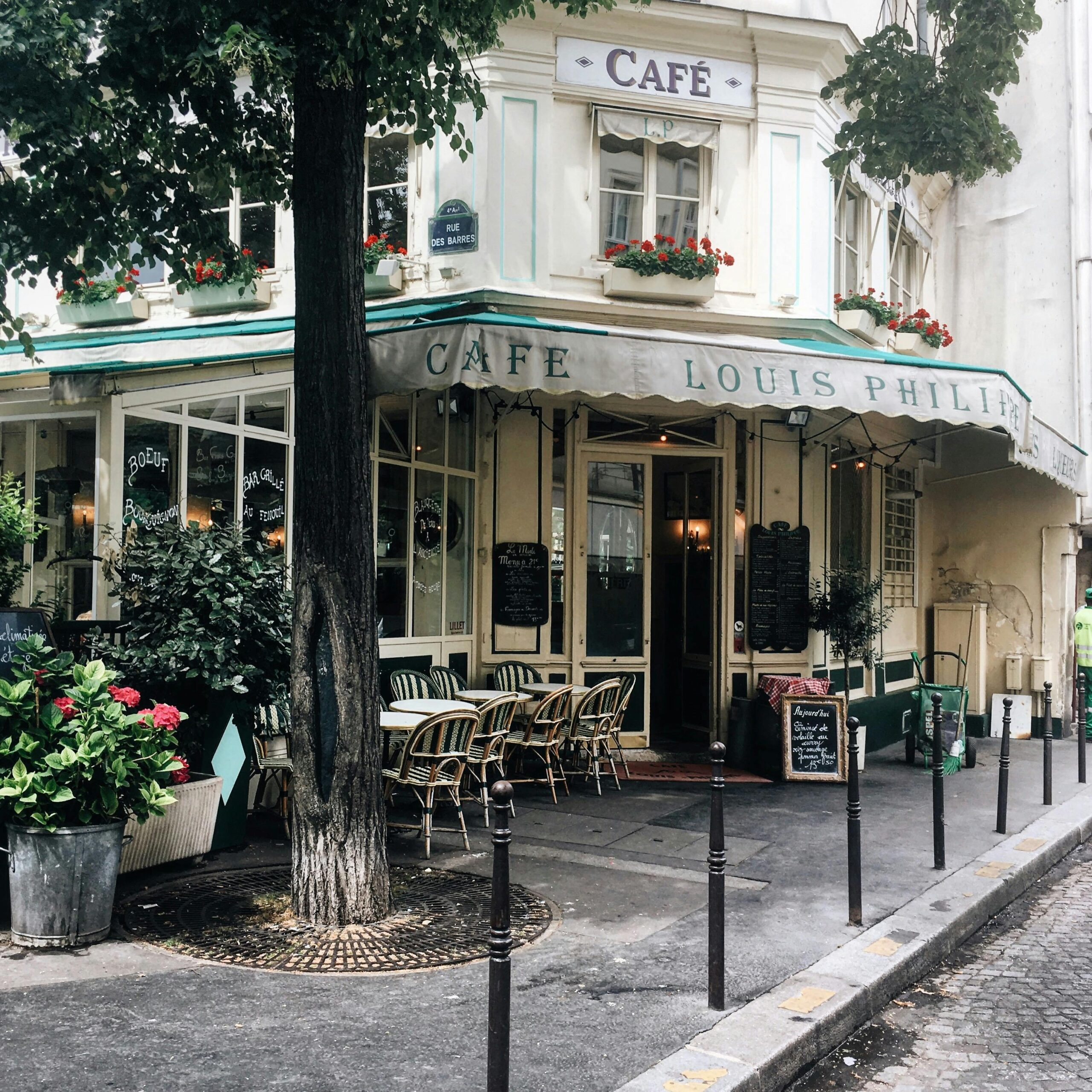 Classic Parisian café with outdoor seating, surrounded by lush greenery and flowers in central Paris.